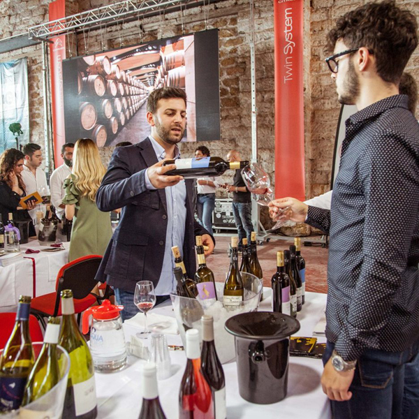 An indoor scene at the Festa Del Vino Chiusi, where a man is serving wine to an attendee